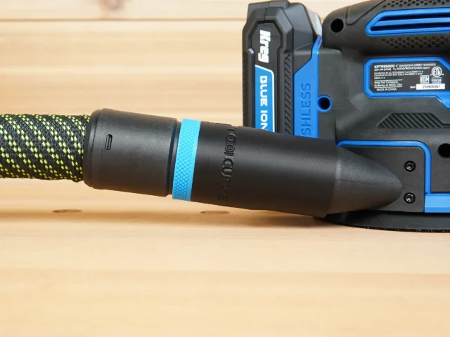 Black hose adapter with blue band attached to a blue and black Kreg random orbit sander, connected to a yellow and black braided hose