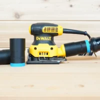 Black 1-1/4" ToolCurve hose adapter with blue ring linking a DeWalt palm sander to an orange vac hose, spare parts beside