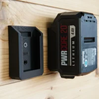 Black 3D-printed battery mount holder for SKIL 20v PWRCORE attached to wooden wall surface, with PWRCORE battery inserted into the mount