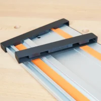 Two black ToolCurve end caps slid onto a Wen aluminum guide rail with orange strips, on a workbench