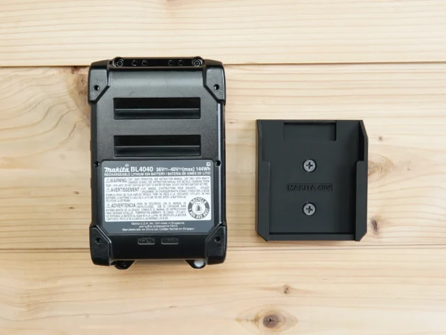 Makita 40v Max XGT battery next to a black plastic wall mount holder showing the slot designed to hold the battery