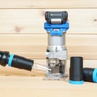 Black 1-1/4 inch ToolCurve hose adapter with blue cuff joining an orange vac hose to a Kreg 20v trim router, two spare adapters beside it