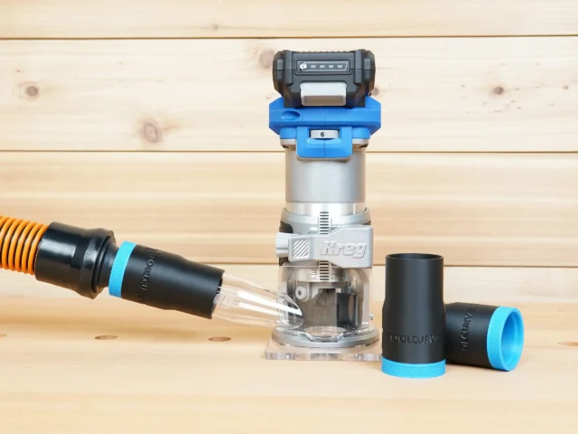 Black 1-1/4 inch ToolCurve hose adapter with blue cuff joining an orange vac hose to a Kreg 20v trim router, two spare adapters beside it