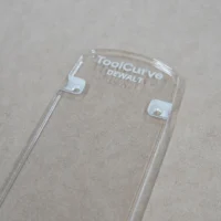 Clear acrylic zero clearance insert for Dewalt 12-inch miter saw, shown from above with two white mounting tabs visible along the sides and ToolCurve and Dewalt branding etched at the top