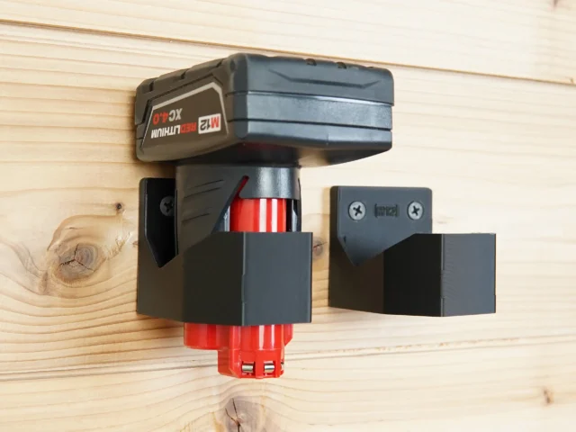 Milwaukee 12v battery mounted in black plastic holder with red battery contacts visible, shown installed on pine wood alongside an unmounted matching holder