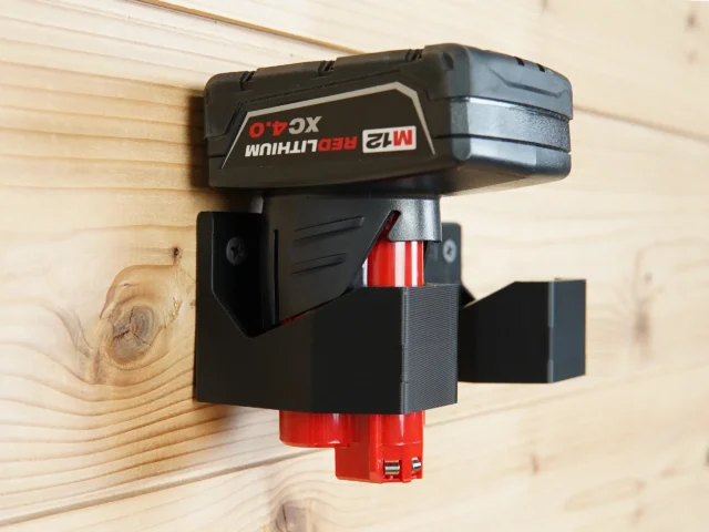 Black battery holder mount with red base, mounted on wood wall with Milwaukee 12v battery inserted and secured