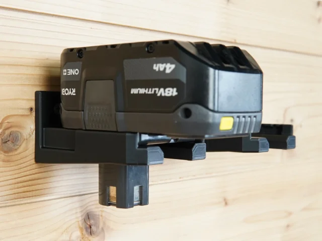 Black plastic battery holder mount with a Ryobi 18v battery clicked into place, mounted on wooden wall studs