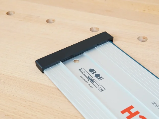 Black PETG protective cap installed on the end of a Bosch guide rail, showing the friction fit grip over the aluminum profile