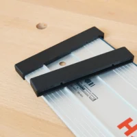 Two black end caps fitted over the end of a Bosch FSN guide rail resting on a beech workbench