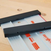 Two black PETG protective end caps slid onto a Mafell aluminum guide rail resting on a wooden benchtop