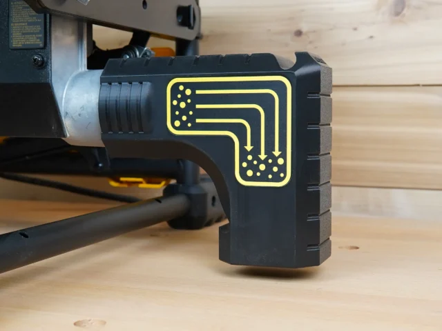 Black plastic dust collection adapter with yellow flow diagram mounted on a DeWalt table saw rear port, showing bucket hanging bracket design