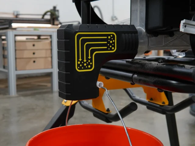 Black plastic bucket adapter with yellow ToolCurve logo attached to DeWalt table saw dust port, with red collection bucket hanging below