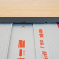 Black protective cap with pink friction strip attached to end of white Mafell guide rail, showing orange branding and alignment hole