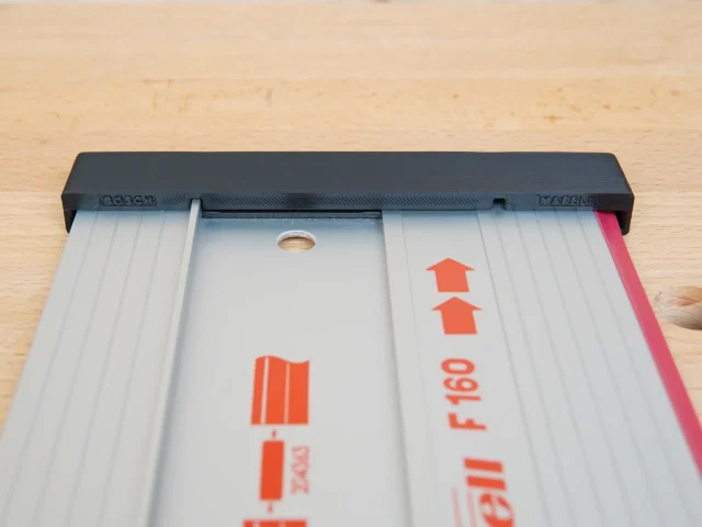 Black protective cap with pink friction strip attached to end of white Mafell guide rail, showing orange branding and alignment hole