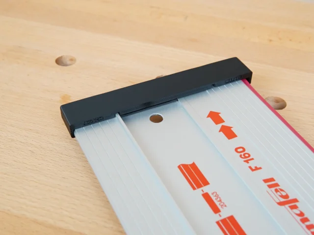 Black protective cap installed on the end of a Mafell guide rail with red branding visible on the white aluminum rail