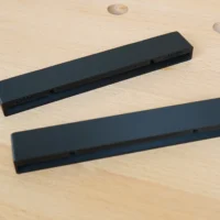 Two black PETG protective caps for Bosch guide rails, shown separately on light wood