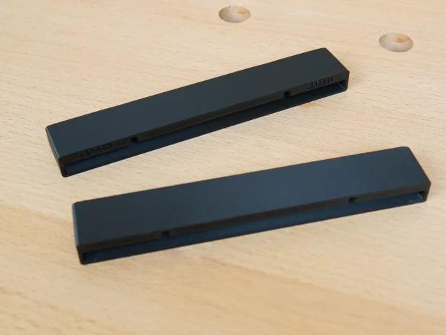 Two black PETG protective caps for Bosch guide rails, shown separately on light wood