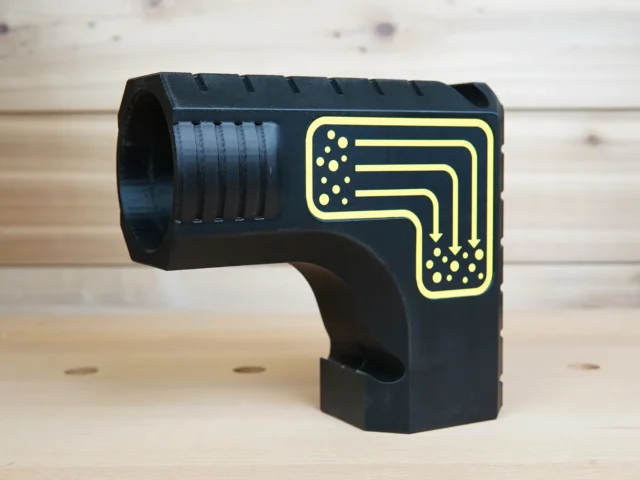 Black plastic DeWalt table saw dust collection adapter with yellow printed circuit diagram, cylindrical port on left side, bucket hanging slot below