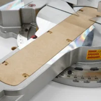 Zero clearance insert mounted on a DeWalt 12-inch miter saw, showing the MDF board aligned with the blade opening and mounting holes
