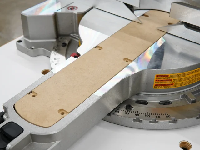 Zero clearance insert mounted on a DeWalt 12-inch miter saw, showing the MDF board aligned with the blade opening and mounting holes