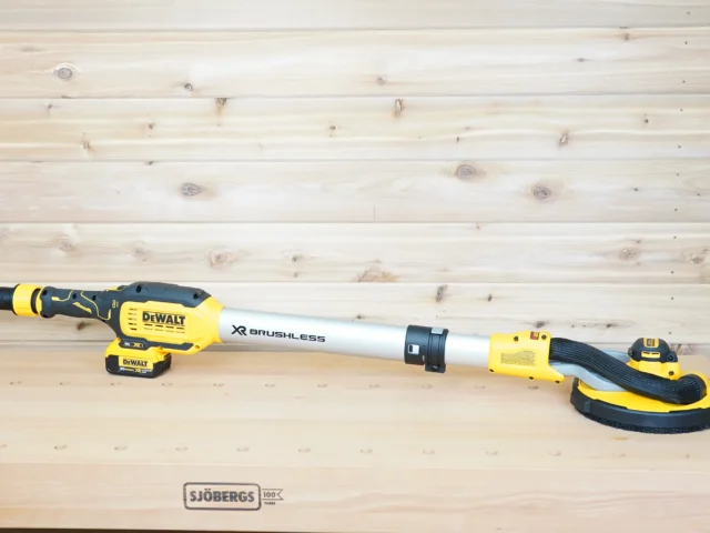 Yellow 1-1/4 inch hose adapter fitted to the dust port of a Dewalt 20v Max 9in drywall sander on a workbench