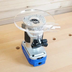 Clear 6-inch round acrylic router base plate mounted on a blue Kobalt trim router on a workbench