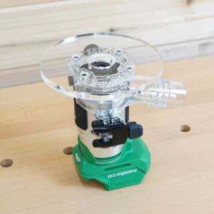 Clear 6-inch round acrylic router base plate with dust port installed on a green Metabo HPT trim router