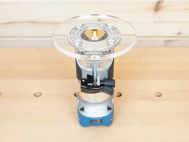 6-inch round clear acrylic router base plate mounted on a Hercules trim router, showing brass bushing and measurement scale