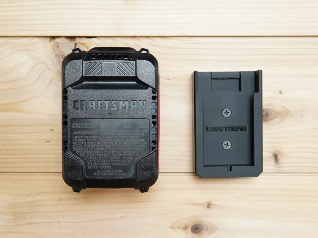 Black plastic battery mount for Craftsman 20v battery shown next to a Craftsman battery on light wood surface