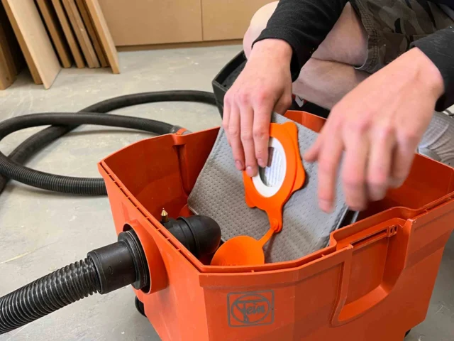 Macam reusable dust bag installed in orange FEIN Turbo dust extractor, showing gray filter material and orange internal components