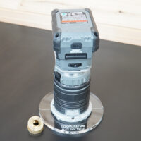 Clear 6 inch round acrylic router base, guide bushing version, mounted on a Flex 24V trim router with a brass threaded bushing nut beside it
