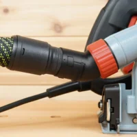 No Snag Dust Port adapter installed on a Mafell track saw, with braided hose and orange twist-lock connector angled upward away from the workpiece