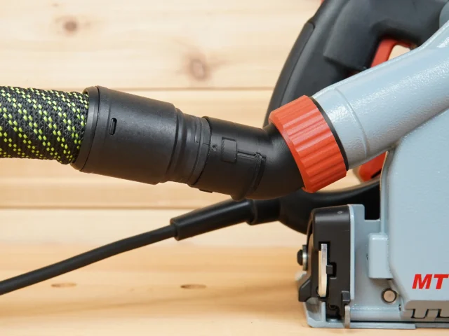 No Snag Dust Port adapter installed on a Mafell track saw, with braided hose and orange twist-lock connector angled upward away from the workpiece