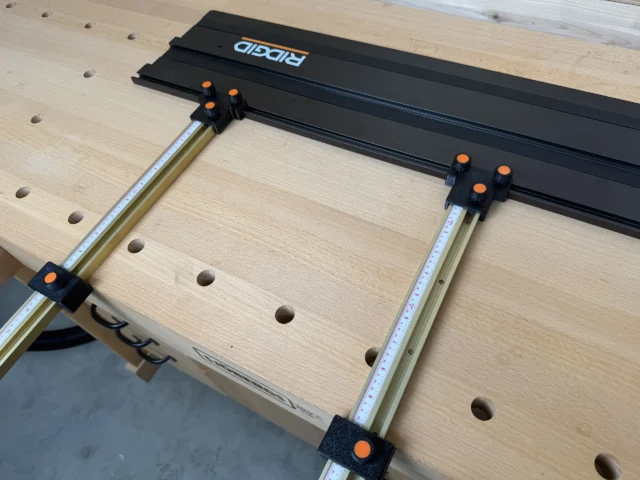 ToolCurve Parallel Guides mounted on Ridgid track saw rails, with black brackets and orange knobs securing dual aluminum guide bars over a workbench with pocket holes