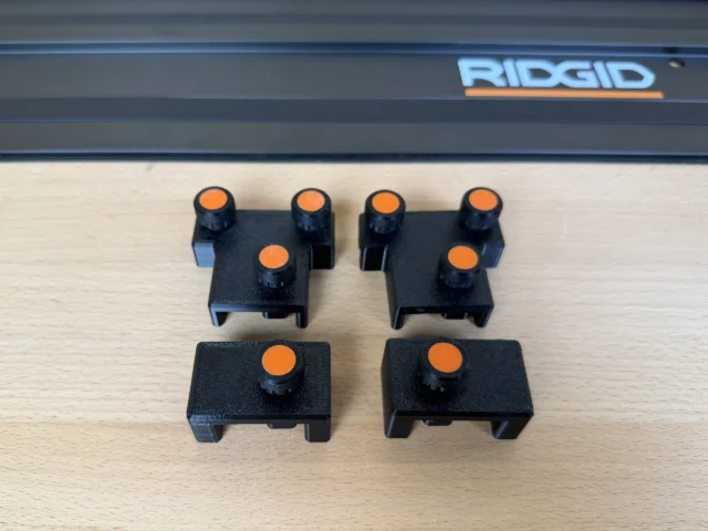 Black plastic parallel guide brackets with orange adjustment knobs, displayed in two rows next to a Ridgid track saw rail