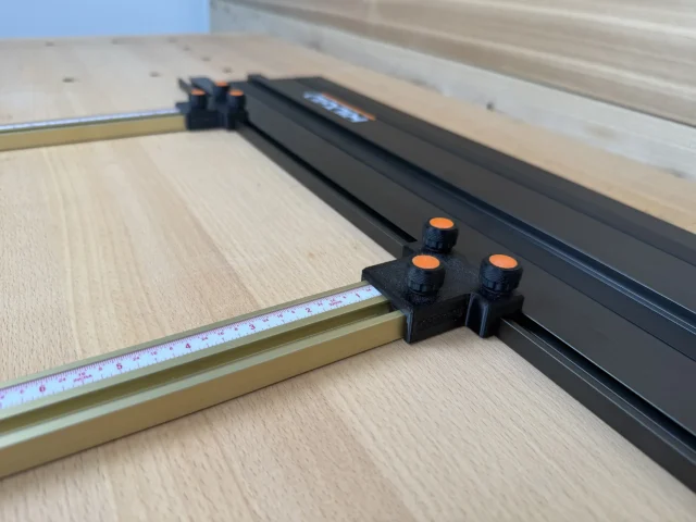 Black plastic parallel guide bracket with three orange knurled knobs mounted on brass-colored Incra T-Track rail, positioned perpendicular to a Ridgid track saw