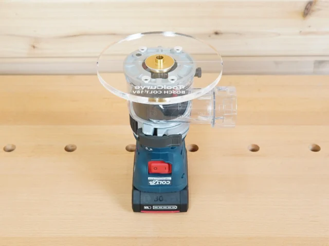 6-inch round clear acrylic base plate attached to a Bosch Colt 18V trim router, mounted on a wood workbench