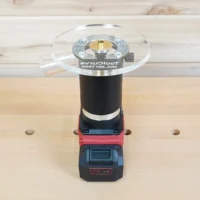6-inch round clear acrylic router base plate mounted on a Skil trim router with battery pack, showing the brass center bushing and guide ring