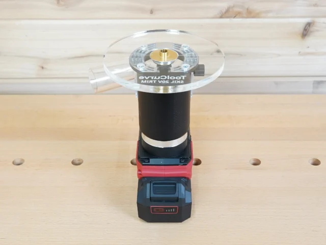 6-inch round clear acrylic router base plate mounted on a Skil trim router with battery pack, showing the brass center bushing and guide ring