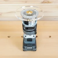 6-inch round clear acrylic router base plate mounted on a Flex 24V trim router, showing brass center collar and mounting holes