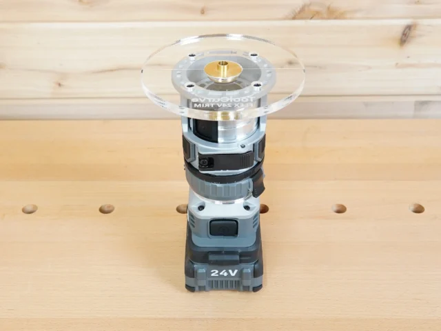 6-inch round clear acrylic router base plate mounted on a Flex 24V trim router, showing brass center collar and mounting holes