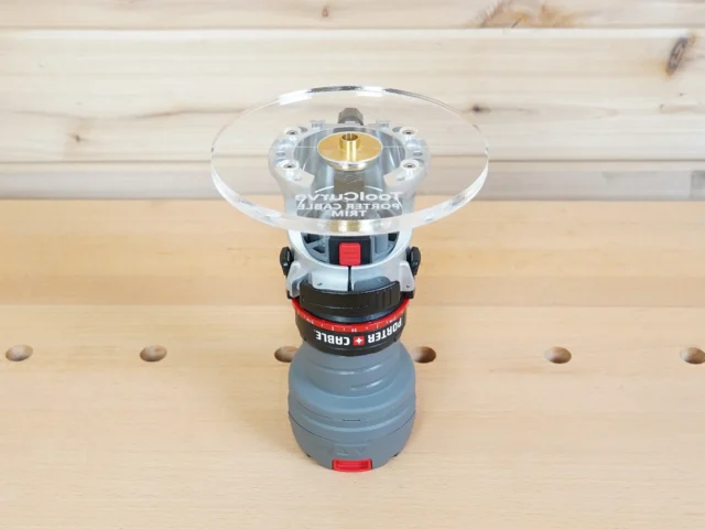 6-inch round clear acrylic router base plate mounted on a Porter Cable trim router, showing the brass center collet and guide bushing hole from above.