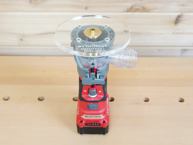 6-inch round clear acrylic base plate mounted on red Craftsman trim router, showing brass center insert and guide bushing port