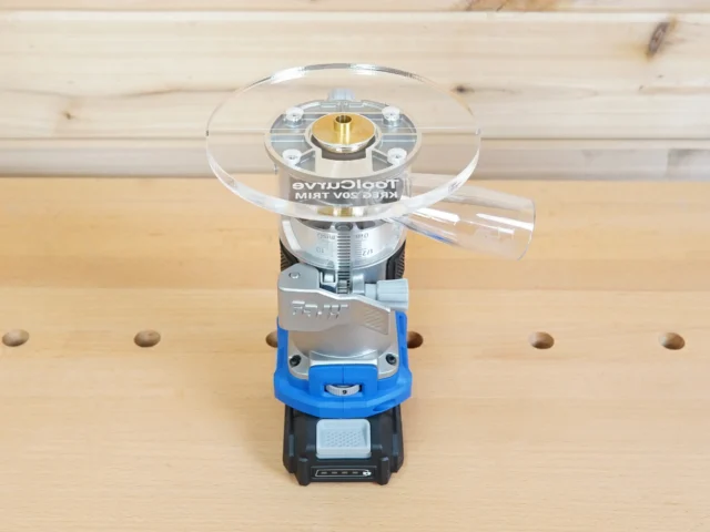 6-inch round clear acrylic base plate mounted on a Kreg trim router with blue housing, shown on a wooden workbench with pegboard