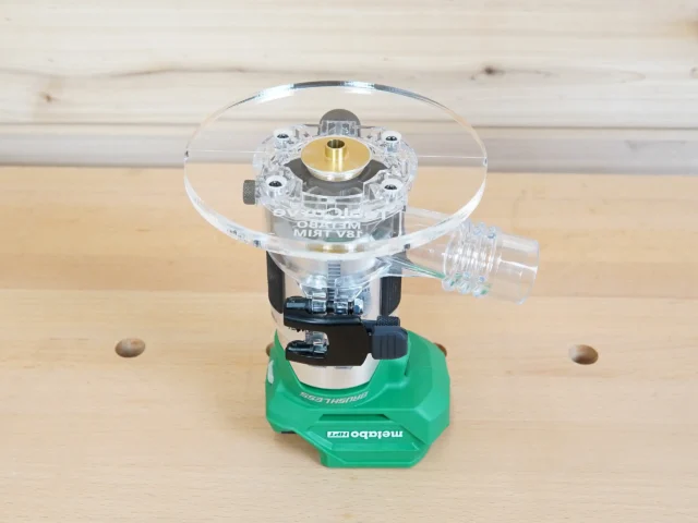 6-inch round clear acrylic base plate with brass center bushing mounted on green Metabo trim router