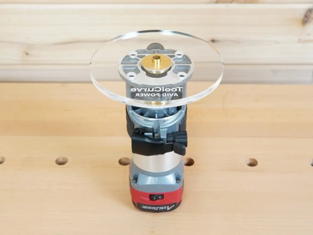 Clear acrylic 6-inch round router base plate mounted on an Avid Power trim router, showing the brass center bushing and mounting hardware from above