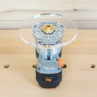 6-inch round clear acrylic base plate mounted on a Wen trim router, viewed from above on a wooden surface