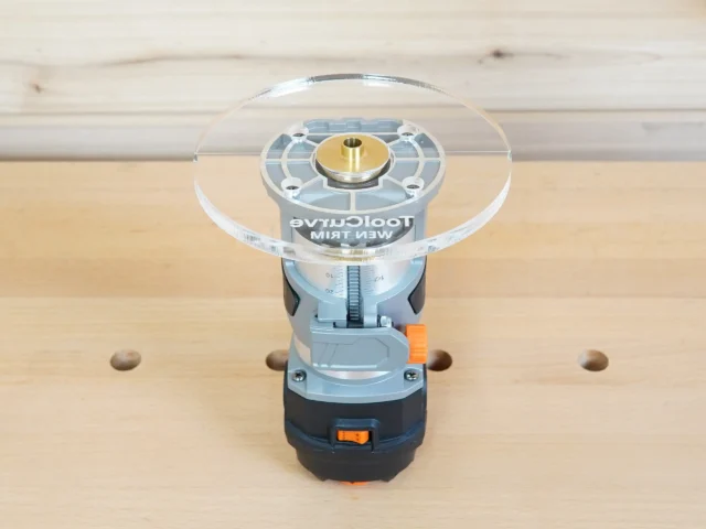 6-inch round clear acrylic base plate mounted on a Wen trim router, viewed from above on a wooden surface