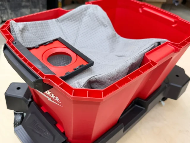 Red Macam reusable dust bag with gray fabric insert inside, displayed empty in a red and black Milwaukee M18 Packout vacuum bin