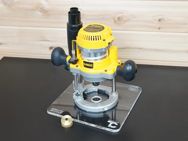 Clear 10-inch square acrylic guide bushing base plate mounted on a yellow Dewalt DW618 plunge router, brass knob beside it